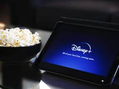 A tablet displaying the Disney+ app with some popcorn beside it.