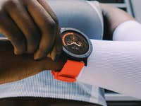 A close-up of a black and orange smartwatch on a wrist, with a person adjusting it.