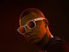 A person wearing white sunglasses against a dark background.