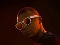 A person wearing white sunglasses against a dark background.