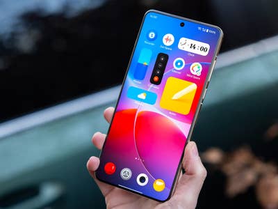 A person holding a OnePlus 13 smartphone displaying a colorful home screen.