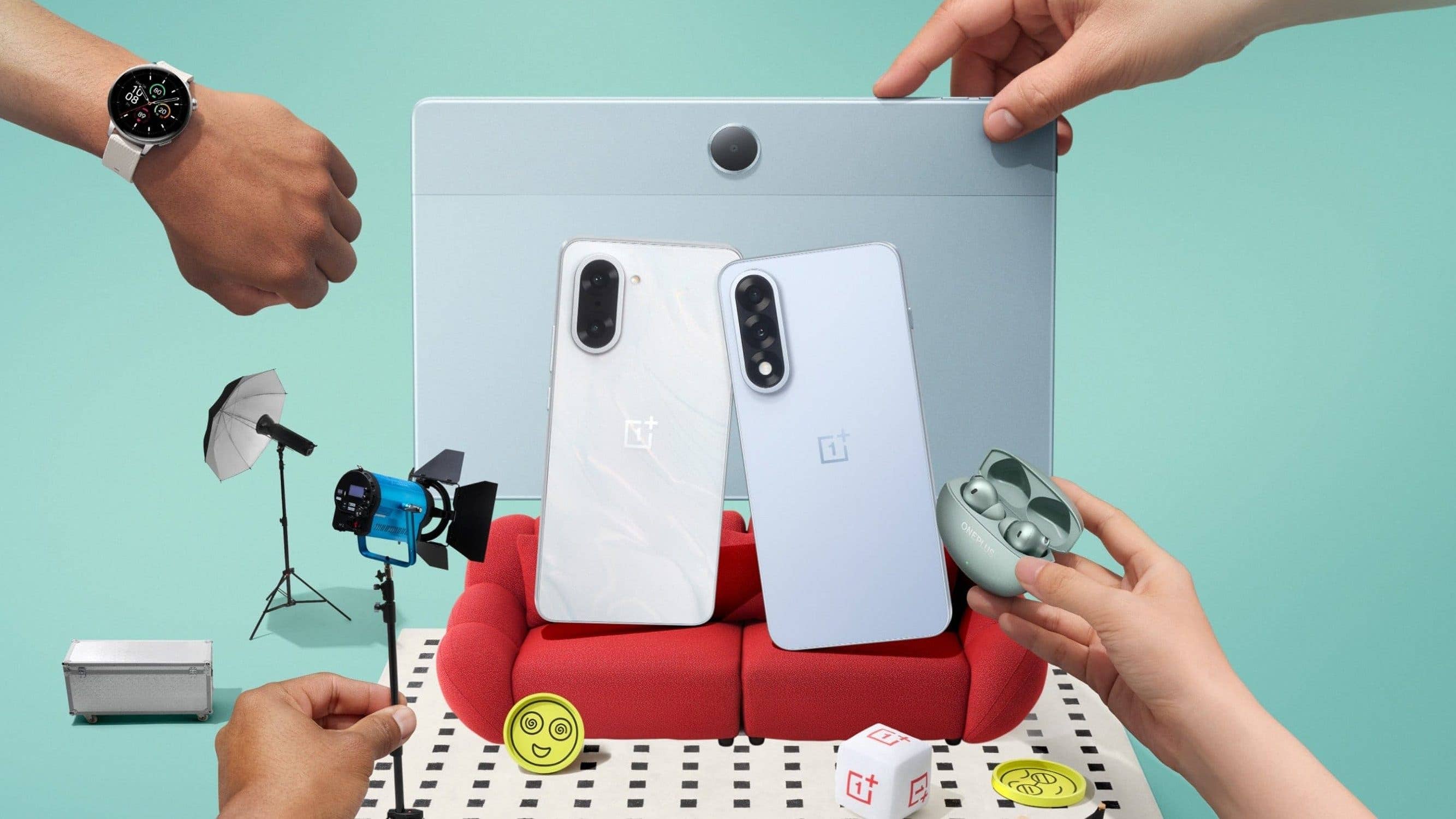 A OnePlus Watch 3 on a wrist, surrounded by a phone, earbuds, and photography equipment.