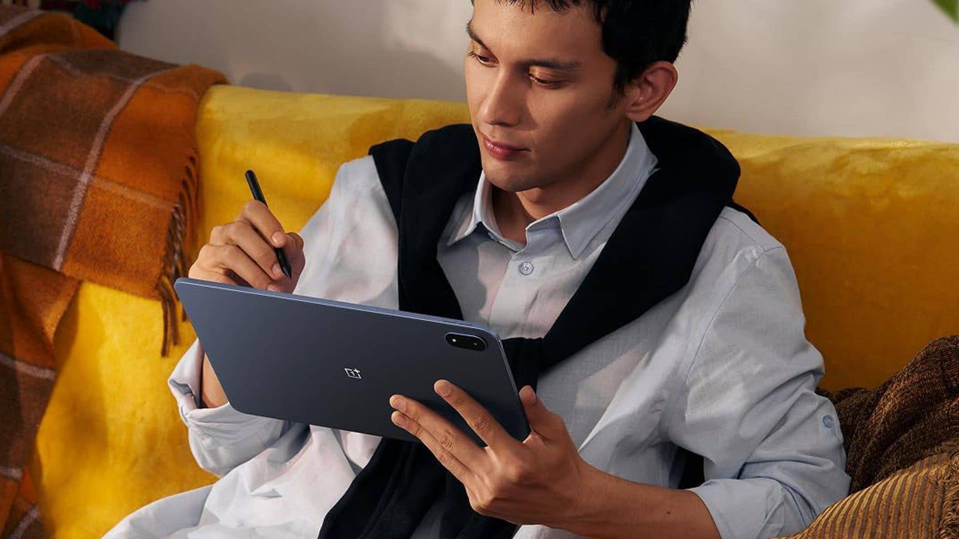 A person sitting on a yellow couch, using a OnePlus Pad with a stylus.