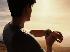 A person checking their OnePlus Watch 3 while enjoying a scenic view at sunset.