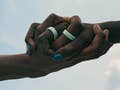 Two hands clasped together, wearing Oura Rings, against a cloudy sky.