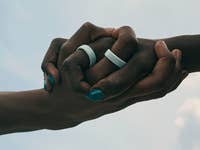Two hands clasped together, wearing Oura Rings, against a cloudy sky.