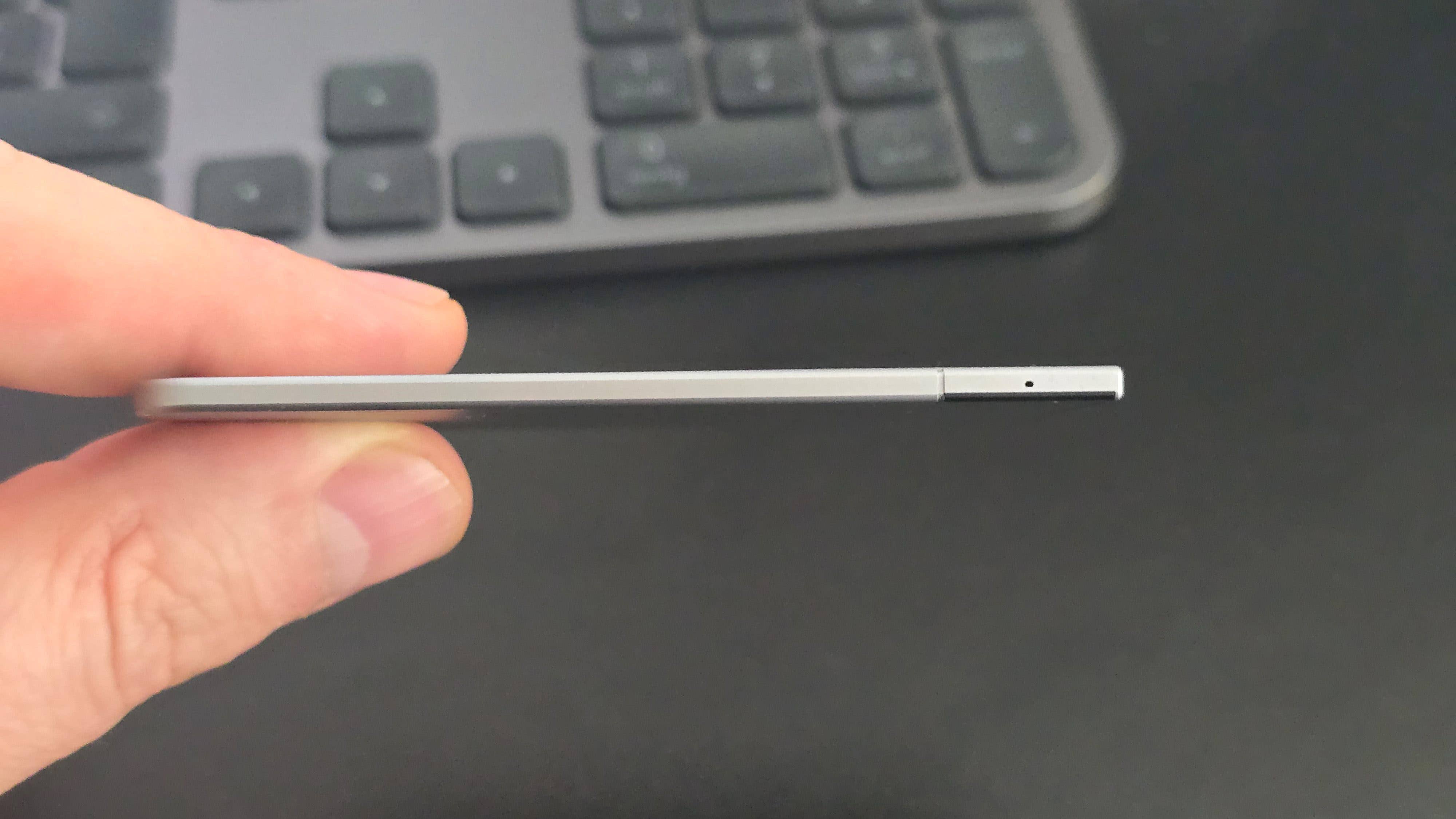 A person holding a slim, silver device with a small hole on one end, background shows a keyboard. A person holding a slim, silver device with a small hole on one end, background shows a keyboard.