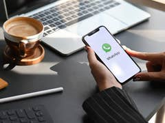 A person holding an iPhone with the WhatsApp logo in the home screen