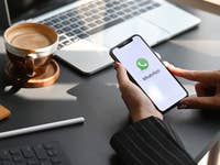 A person holding an iPhone with the WhatsApp logo in the home screen