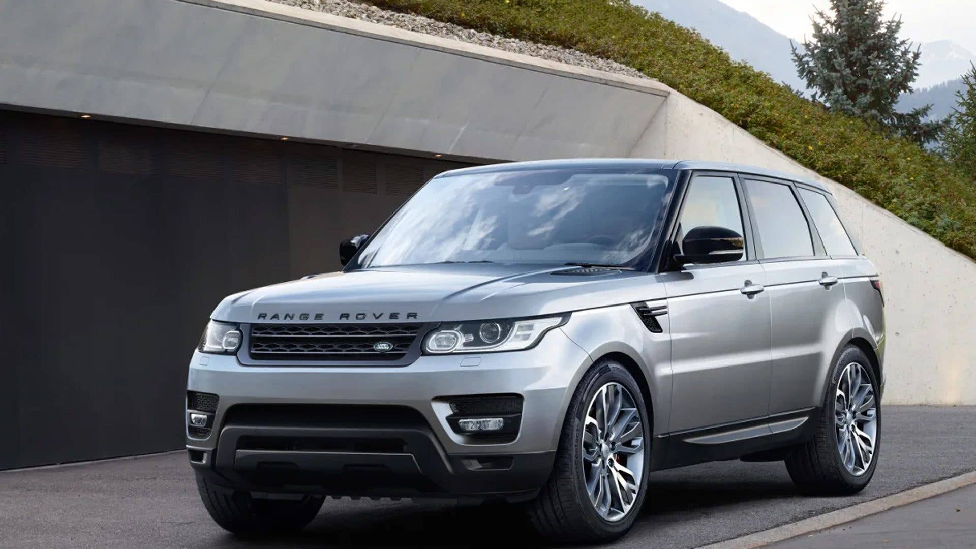 A silver Range Rover parked in front of a modern building with greenery.