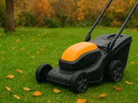 A lawn mower on green grass with fallen leaves, ready for winter preparation.