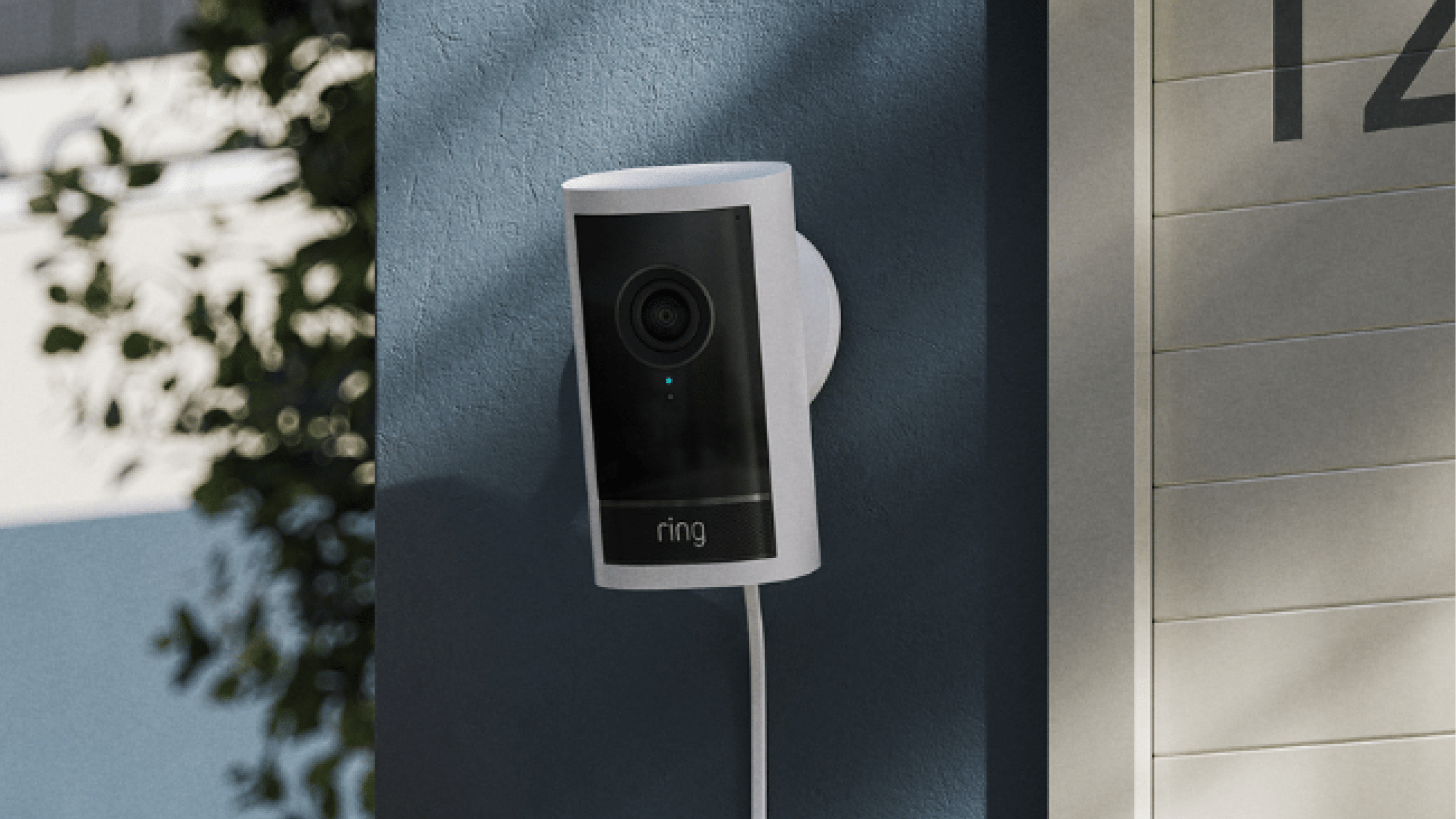 A Ring Outdoor Camera Plus mounted on a blue wall near a house number sign.