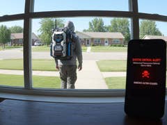 A person with a backpack is seen through a window, while a phone displays a critical alert message.