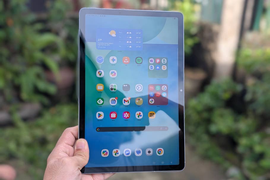 A person holding a Samsung Galaxy Tab S10 FE displaying various app icons on its screen.
