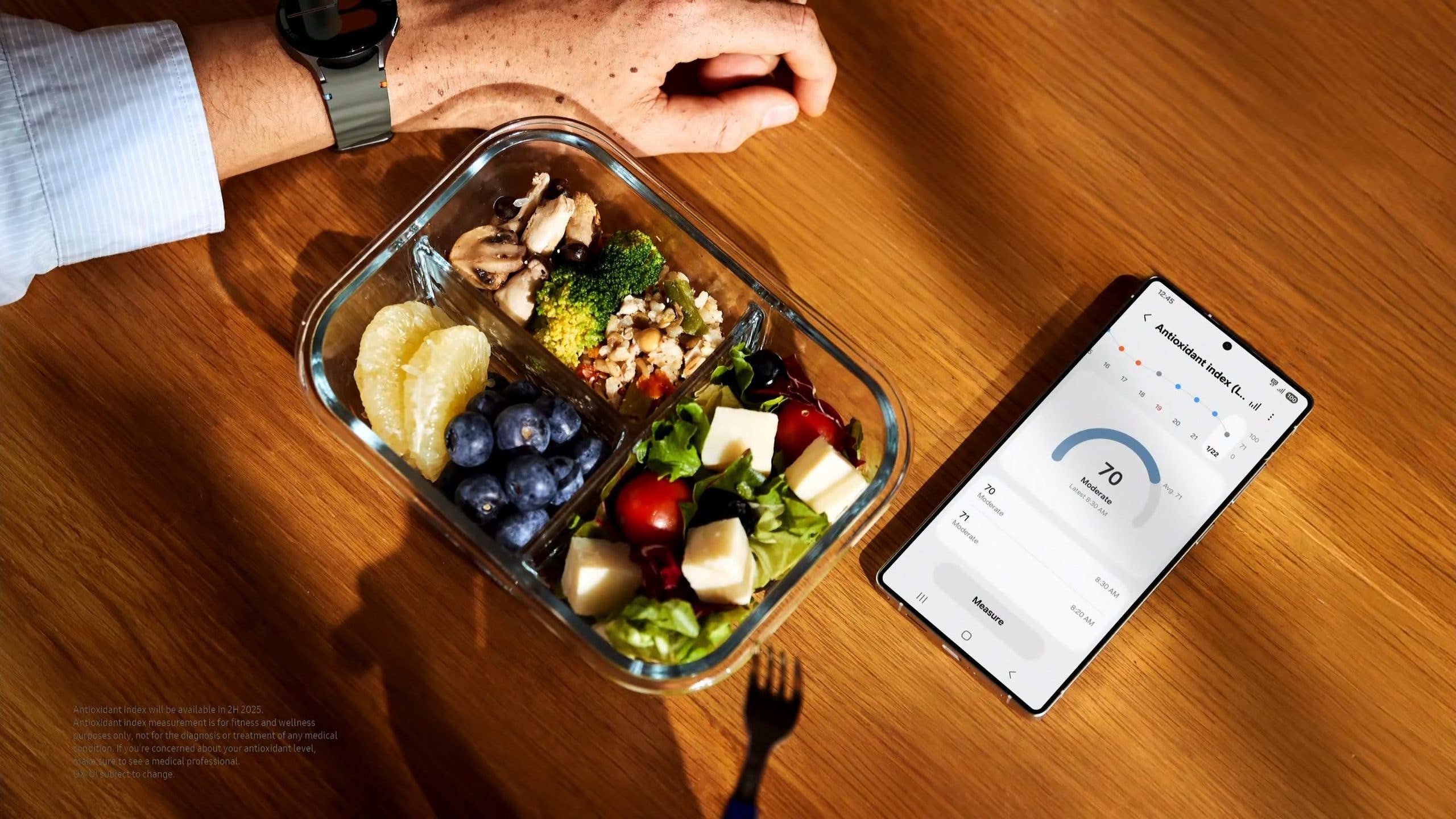 A hand rests next to a healthy meal and a Samsung phone displaying health metrics.