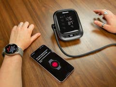 A digital Blood Pressure Monitor side by side with a Samsung Galaxy S23 and the Galaxy Watch 5 Pro