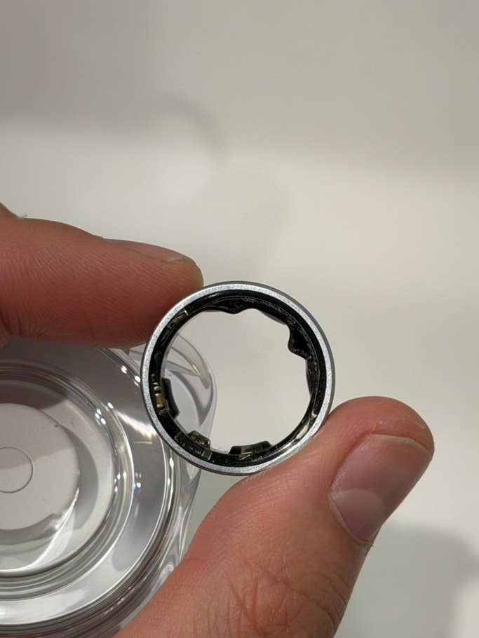 A person holding a Samsung Galaxy ring with a metallic design and an open interior.