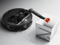 Roborock Saros Z70 robot vacuum with a robotic arm depositing an object into a white container.