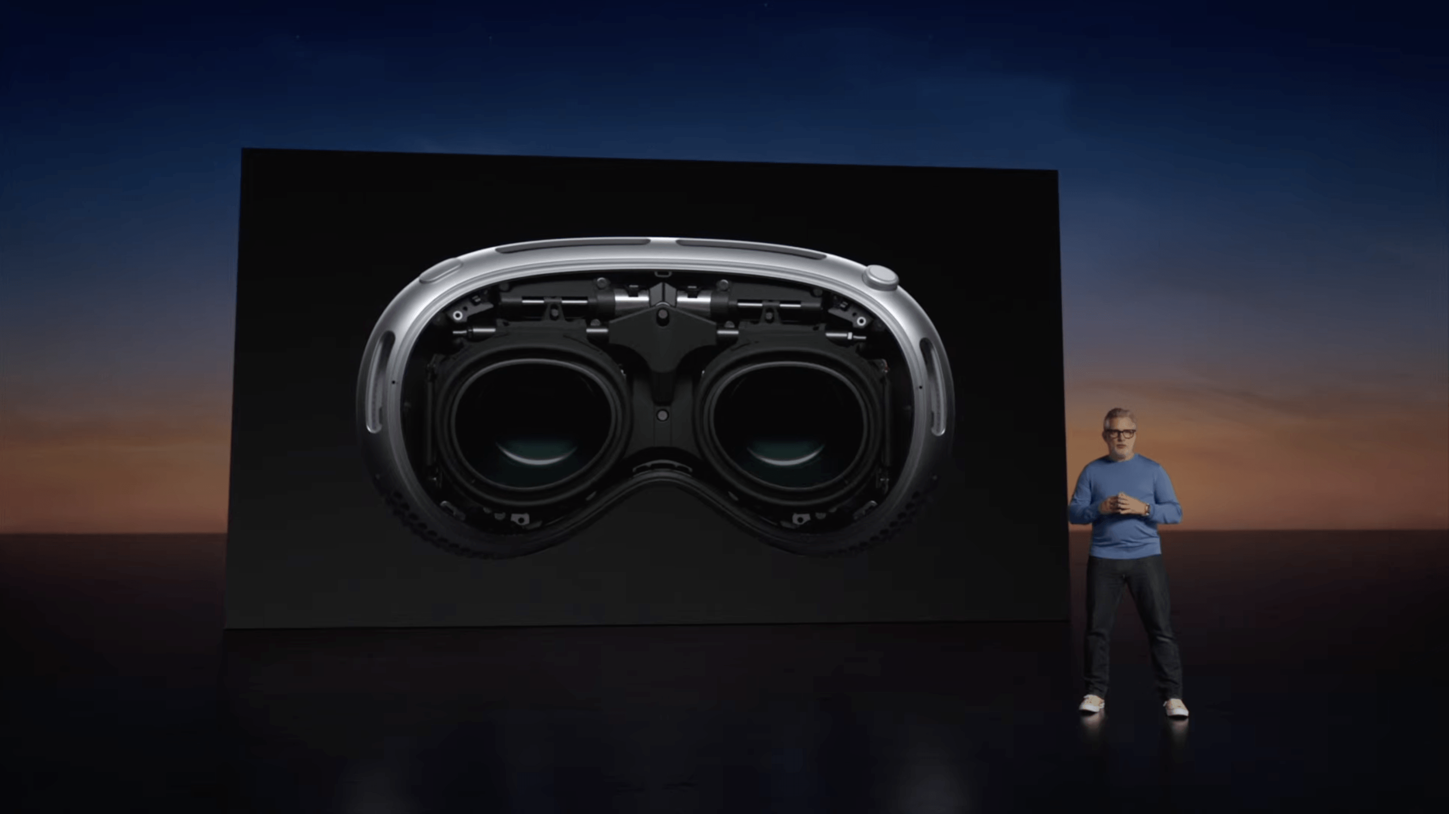 A speaker presents the Apple Vision Pro headset on stage, displayed on a large screen behind.