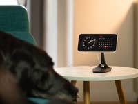 An iPhone displayed on a table, showcasing the Smart Display feature of iOS 17, while a dog lounges on the couch.