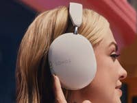 A woman wearing Sonos Ace headphones, touching the ear cup with her fingers.