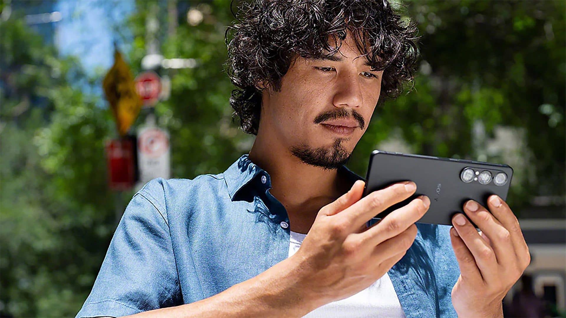 A man with curly hair using a Sony Xperia 1 VII smartphone outdoors.