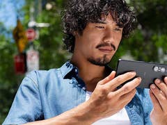 A man with curly hair using a Sony Xperia 1 VII smartphone outdoors.
