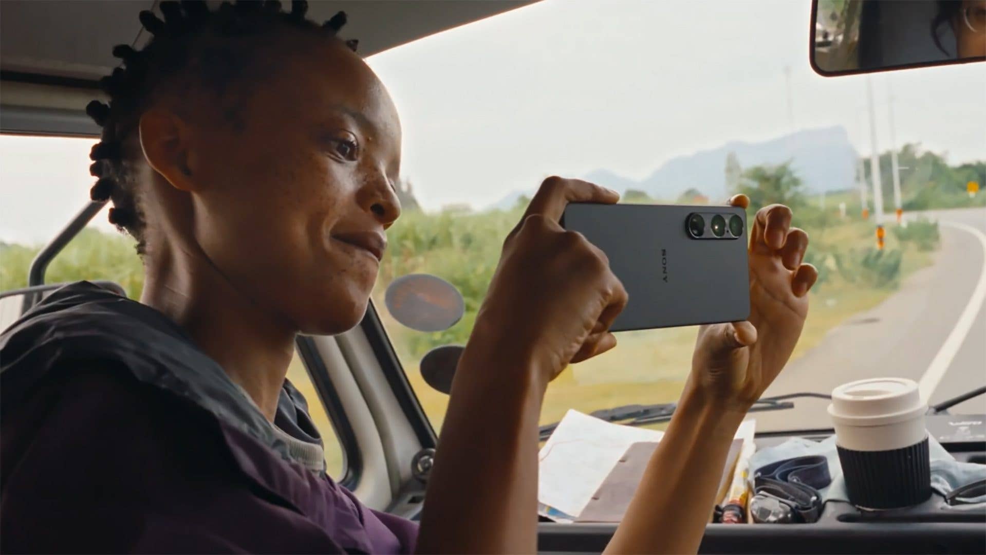 A person in a vehicle holding a Sony Xperia 1 VII smartphone, smiling while taking a photo.