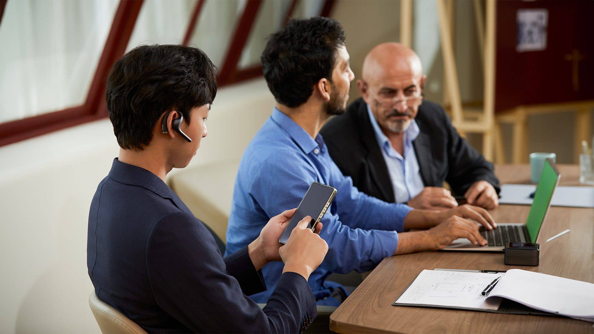Three men in a meeting, one on a phone, using Timekettle W4 Pro for communication.