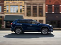 A blue Toyota RAV4 driving past historic buildings on a street.