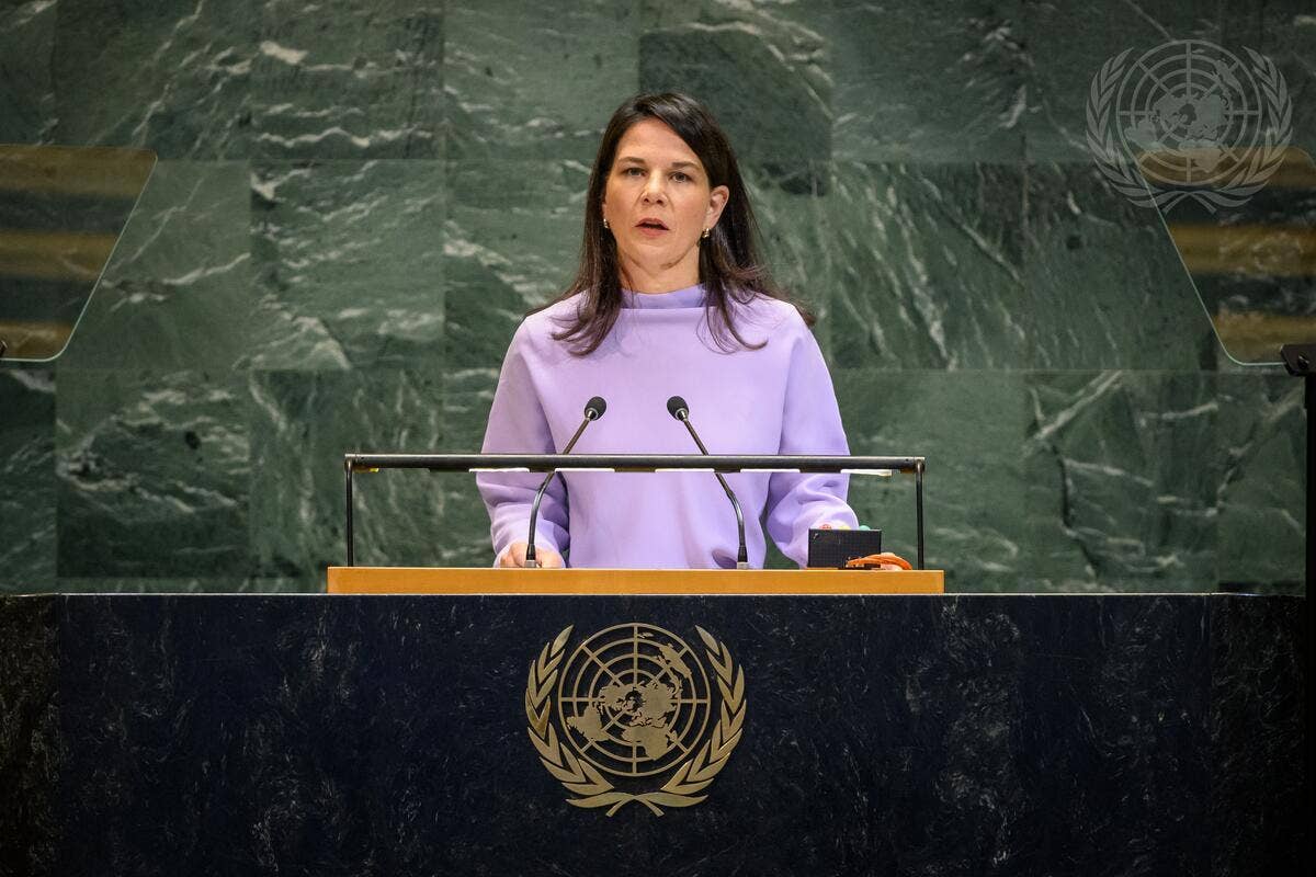 A woman in a purple top speaking at a podium with the UN emblem in the background.