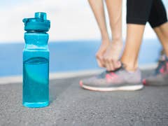 A blue water bottle sits on the ground, with a person tying their shoelaces in the background.