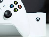 An Xbox controller in white with colorful buttons next to an Xbox box.