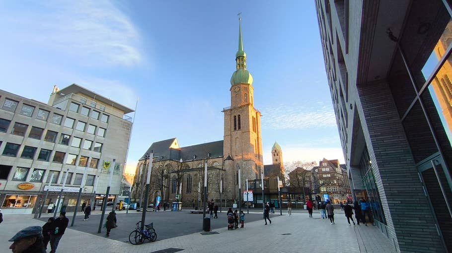 A historic church with a green tower located at a busy square with passers-by.