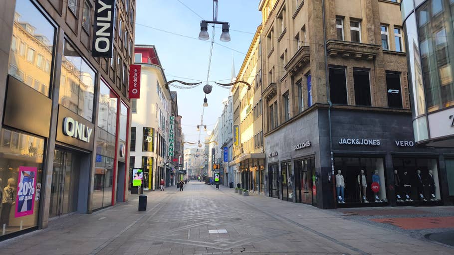 A quiet shopping street with closed shops, including Only and Jack u0026 Jones, on a sunny day.