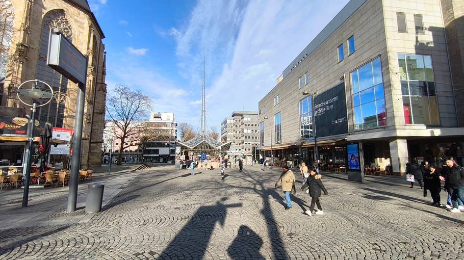 A busy pedestrian square with shops and cafes, a church on the left and many pedestrians.