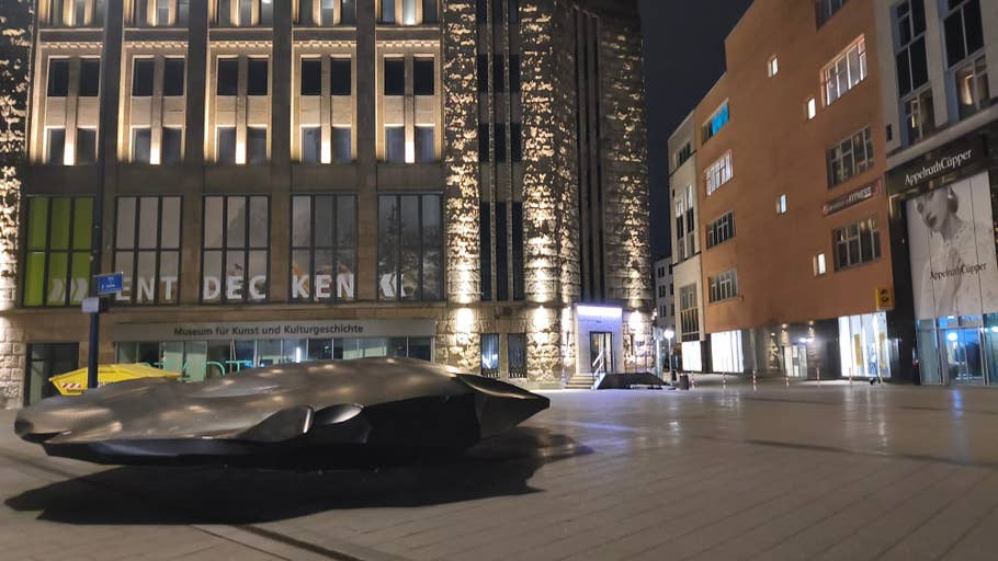 A modern sculpture in front of a museum building at night, with illuminated architecture.