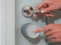 A person using a Yale Linus Smart Lock L2 Lite on a door, pressing a button.