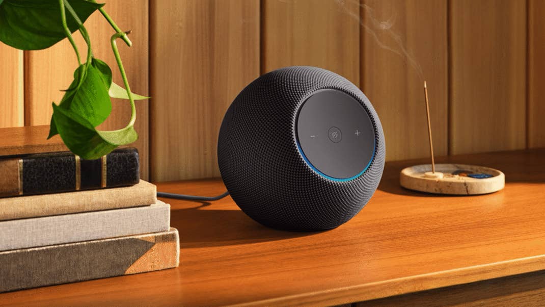 A black Amazon Echo Studio speaker on a wooden surface with books and a plant in the background. A black Amazon Echo Studio speaker on a wooden surface with books and a plant in the background.