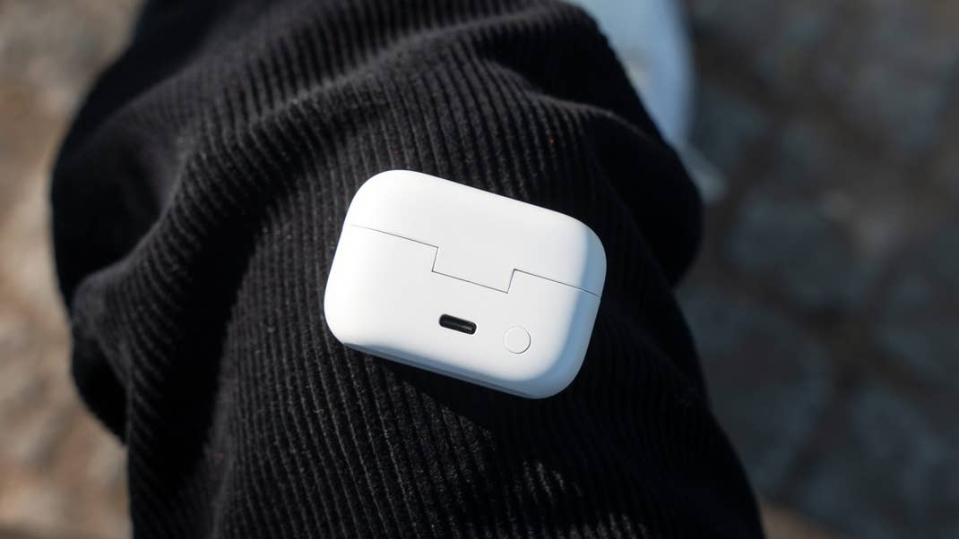 A white charging case for earbuds resting on a black textured surface.