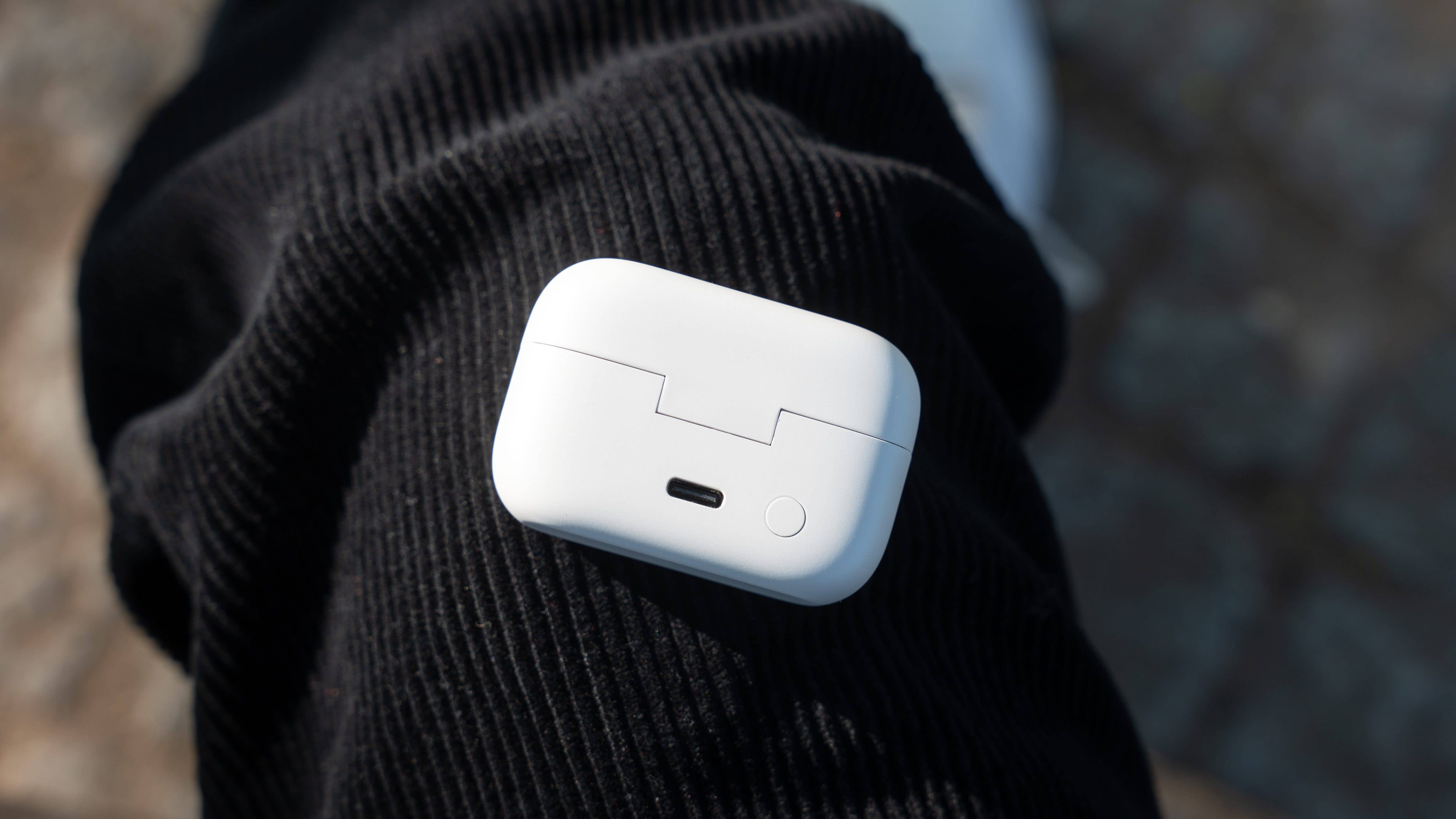 A white charging case for earbuds resting on a black textured surface.