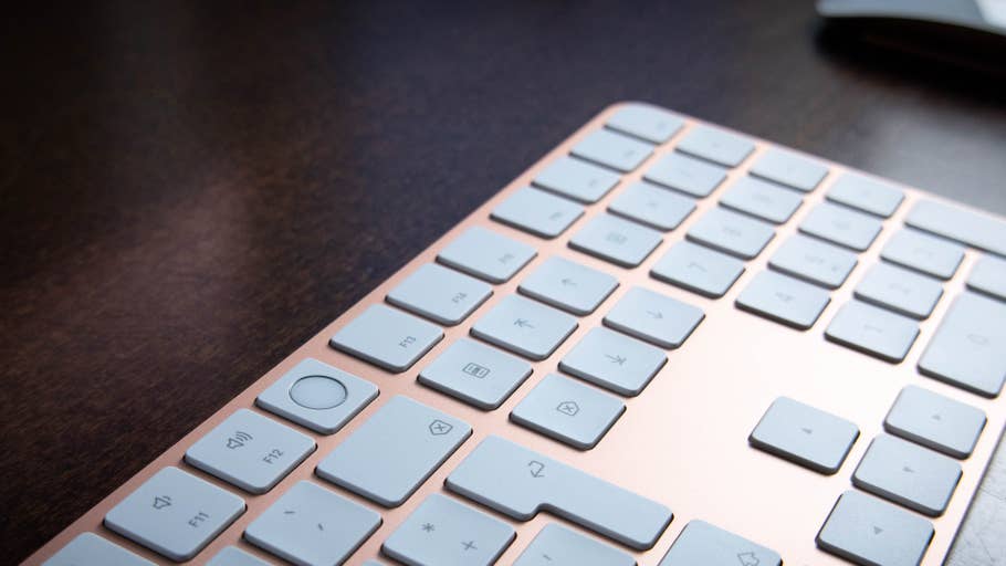 Close-up of an Apple keyboard with light gray keys on a wooden surface.