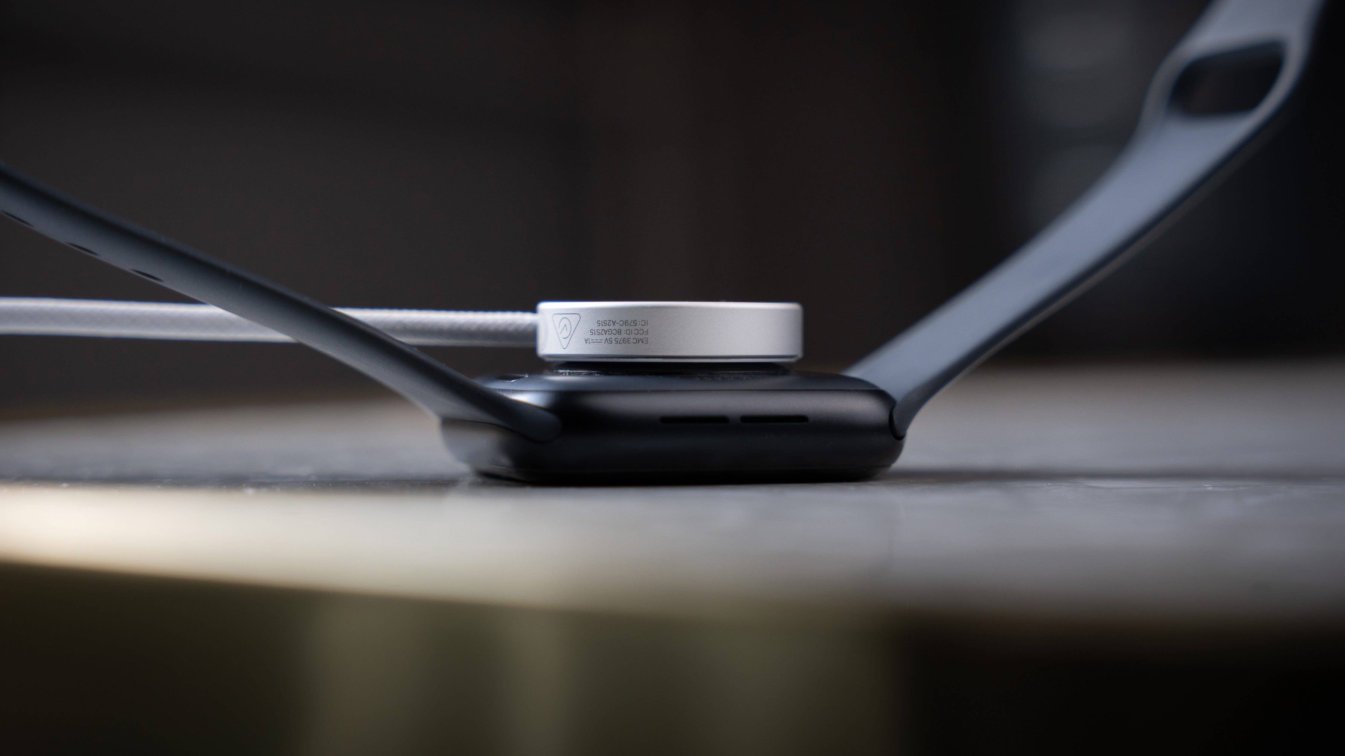 Apple Watch SE 3 charging on a surface with a black strap and silver charger.