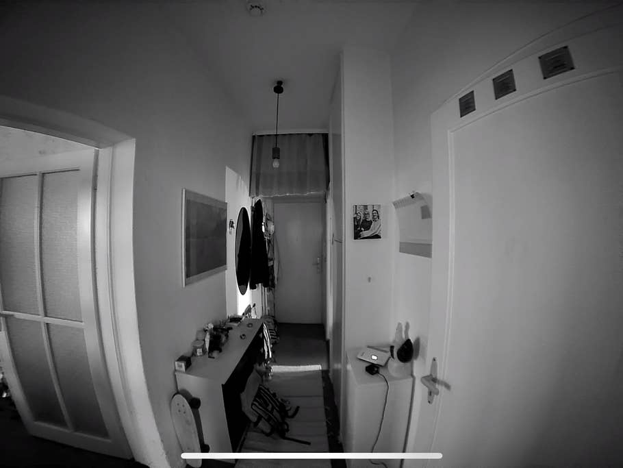 A hallway with a white door, coat rack, and a shelf with items in a black and white tone.