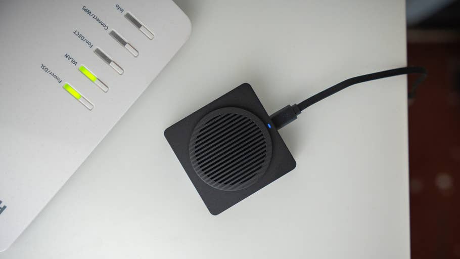 Aqara Doorbell Camera Hub G410 placed next to a modem, featuring a square design and a visible power indicator.