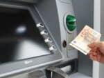 A person using an ATM to withdraw cash, holding a 50 euro banknote.