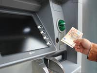 A person using an ATM to withdraw cash, holding a 50 euro banknote.