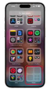 Nagivate to the left most of the home screen and scroll down to the bottom to see the Hide folder. Tap on it and then authenticate to access locked and hidden apps. iPhone displaying the App Library in iOS 18 with various app folders and a highlighted u0027Hiddenu0027 folder.
