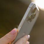 The iPhone 16 Pro remains virtually unchanged in terms of design. A person holds an iPhone 16 Pro showing its camera and side buttons in sunlight.