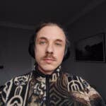 The front camera can take good photos with enough light... A person wearing headphones with a patterned fleece jacket and sitting indoors.